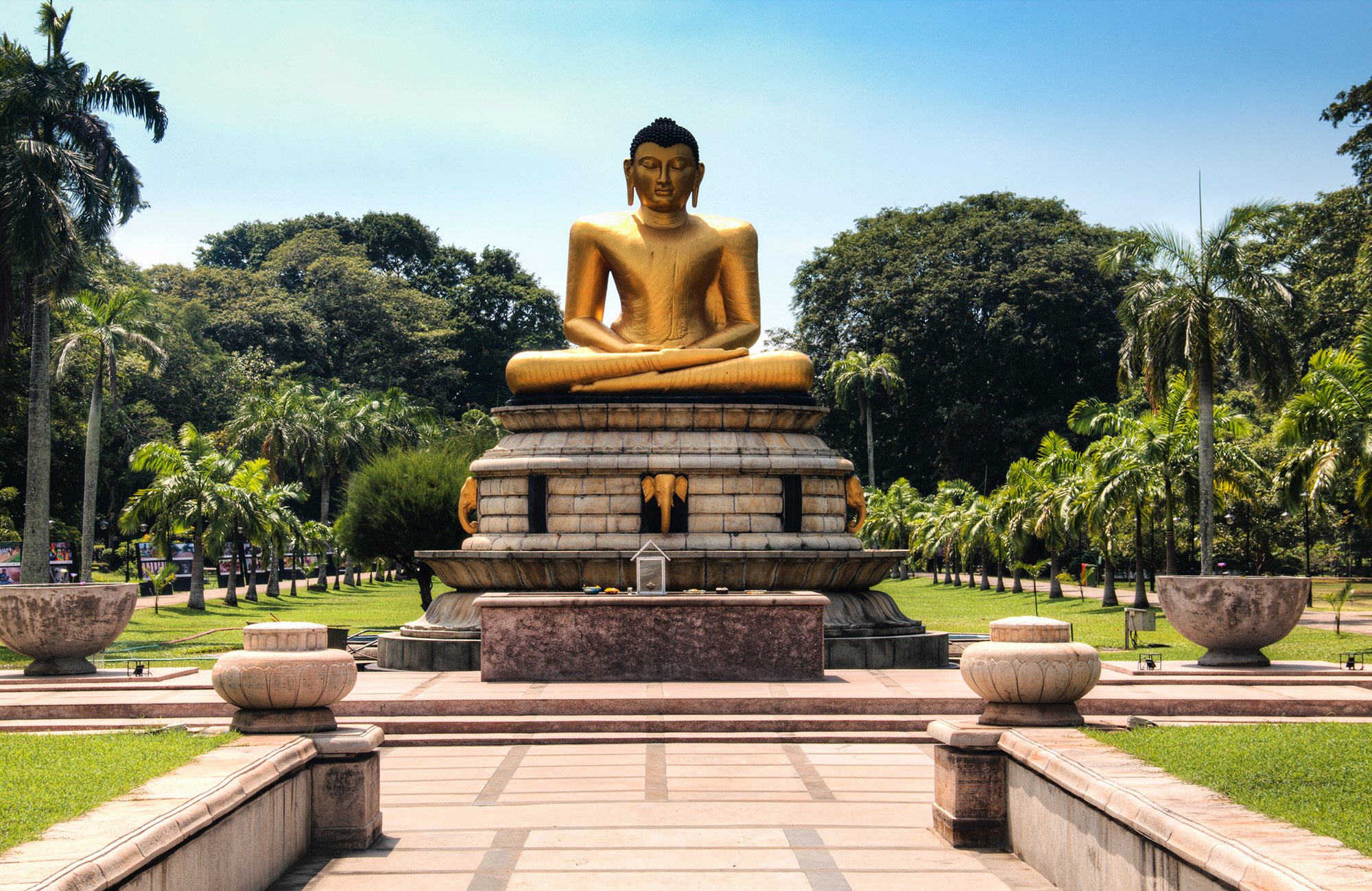 Gouden Boeddhabeeld in Viharamahadevi Park, Colombo, Sri Lanka, omgeven door groene tuinen en bomen