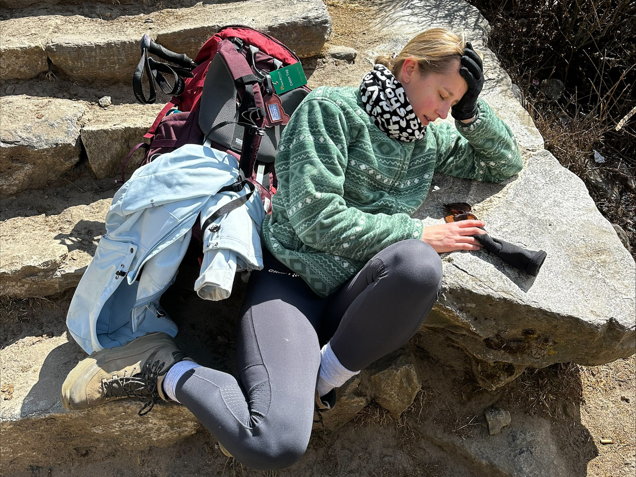 Vermoeide hiker zit uitgeput op een stenen trap met een zware rugzak en wandelstokken naast zich.