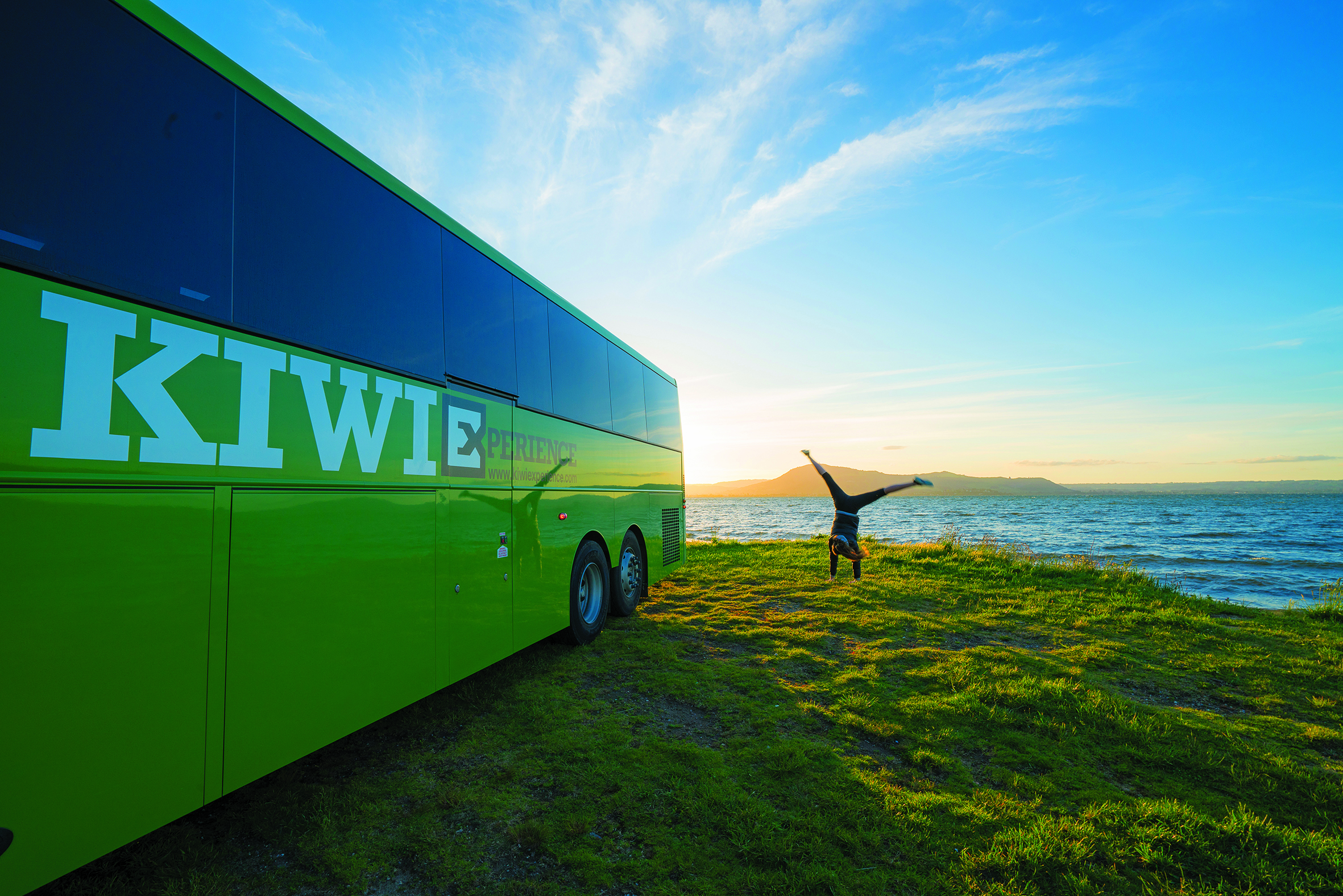 Image of a woman doing a handstand next to a Kiwi Experience bus in New Zealand - KILROY