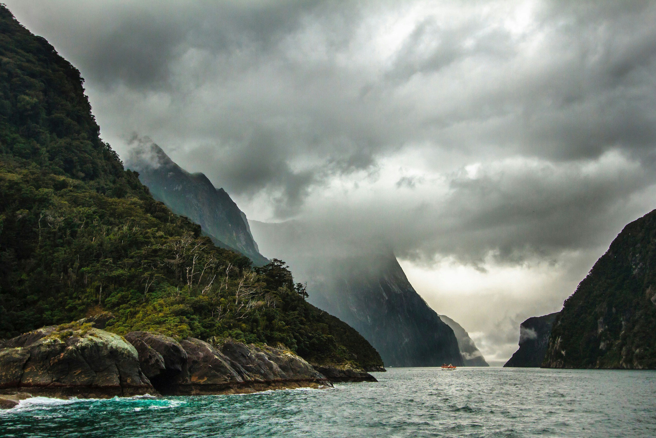 Zware wolken hangen boven de fjorden van Milford Sound, met een boot in de verte.